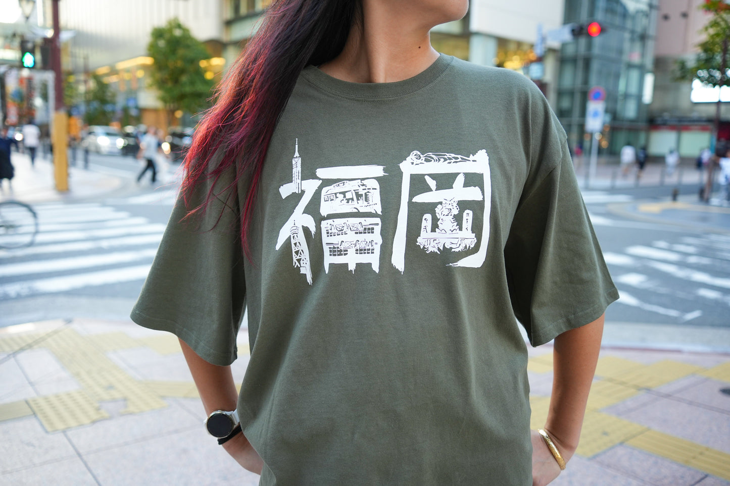 Person wearing a green t-shirt with white graphics and text in urban Fukuoka City